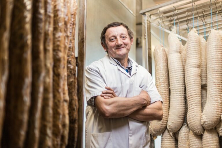 portrait métier de boucher entre un étalage de charcuterie