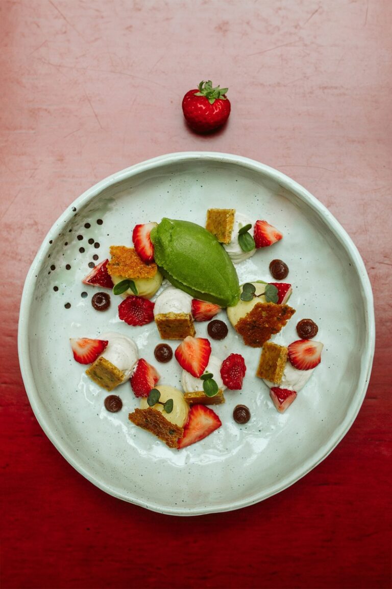 Plat de dessert coloré et texturé composé de fraises, de framboises et d'un sorbet vert, disposés avec soin sur une assiette artisanale, capturé dans un style de photographie culinaire professionnel