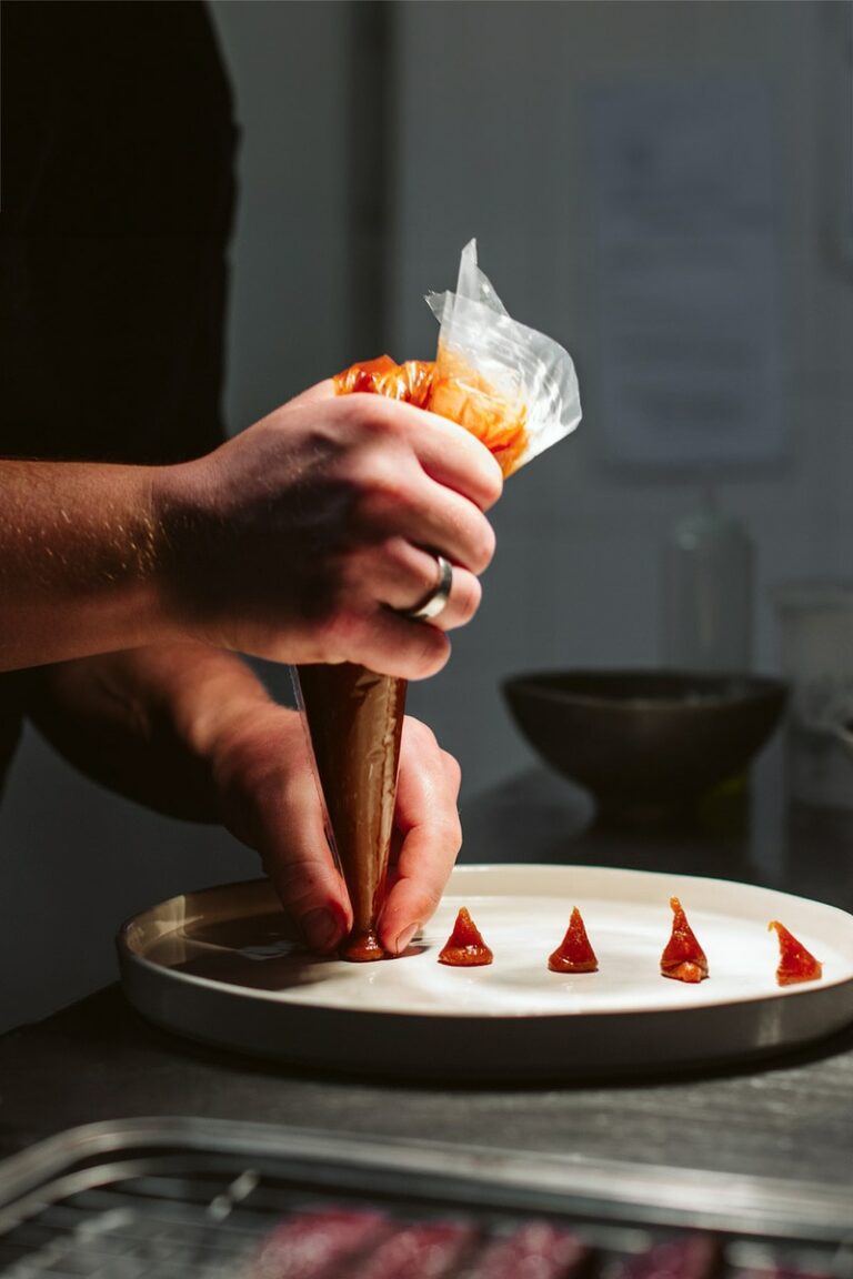 Photographie d'un chef en pleine action décorant méticuleusement un plat avec une sauce rouge, démontrant la précision et l'art de la présentation en cuisine