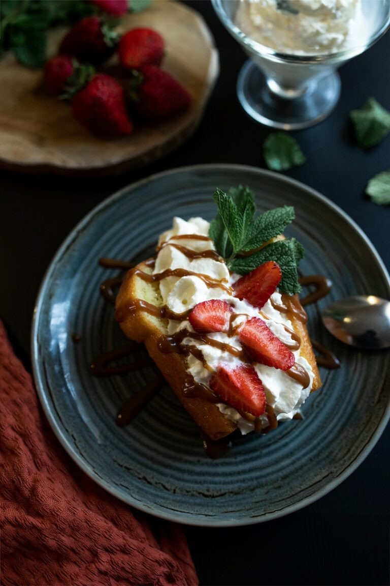 Photographie de haute cuisine d'un éclair garni de crème, de fraises tranchées et de filets de caramel, présenté sur une assiette céramique bleue, évoquant une atmosphère gourmande