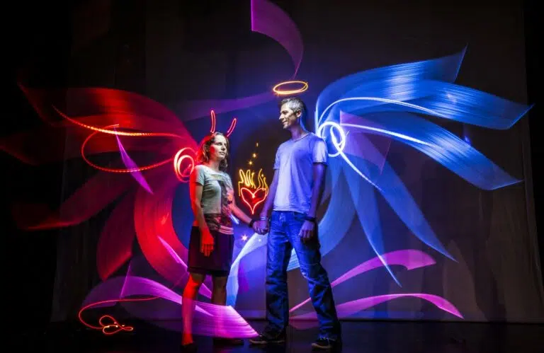 Un couple se tient la main sous des formes dynamiques et colorées réalisées en light painting, créant une ambiance romantique avec un coeur lumineux entre eux