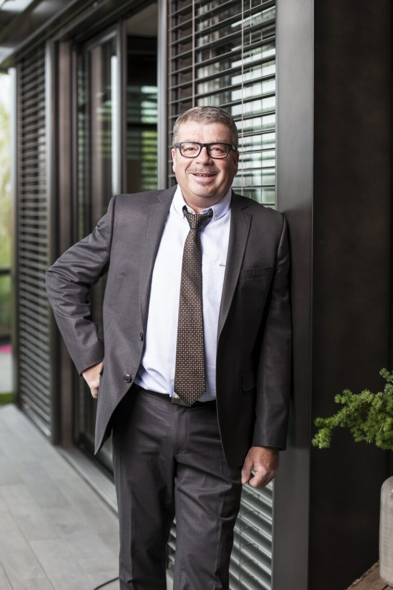 chef d'entreprise en costume gris avec chemise blanche et cravate, souriant dans un showroom