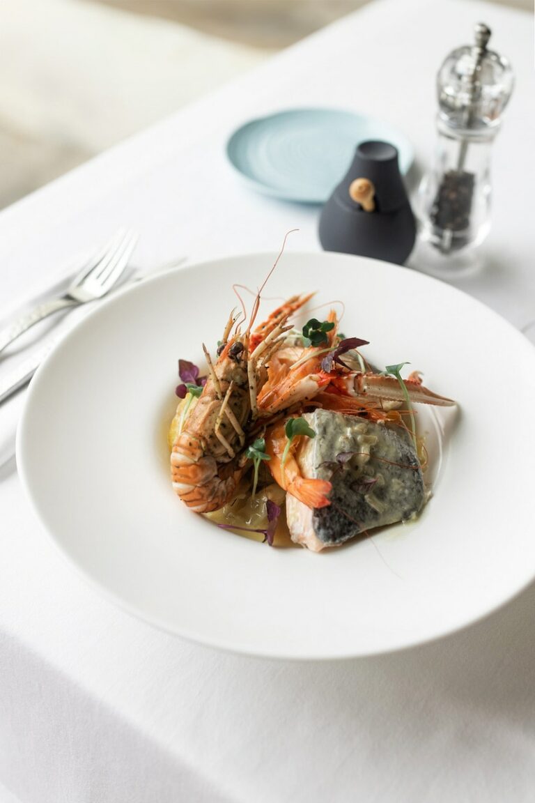 Photographie culinaire d'un plat de fruits de mer gastronomique, mettant en scène des langoustines et un filet de poisson sur un lit de légumes, capturée dans un cadre élégant de restaurant