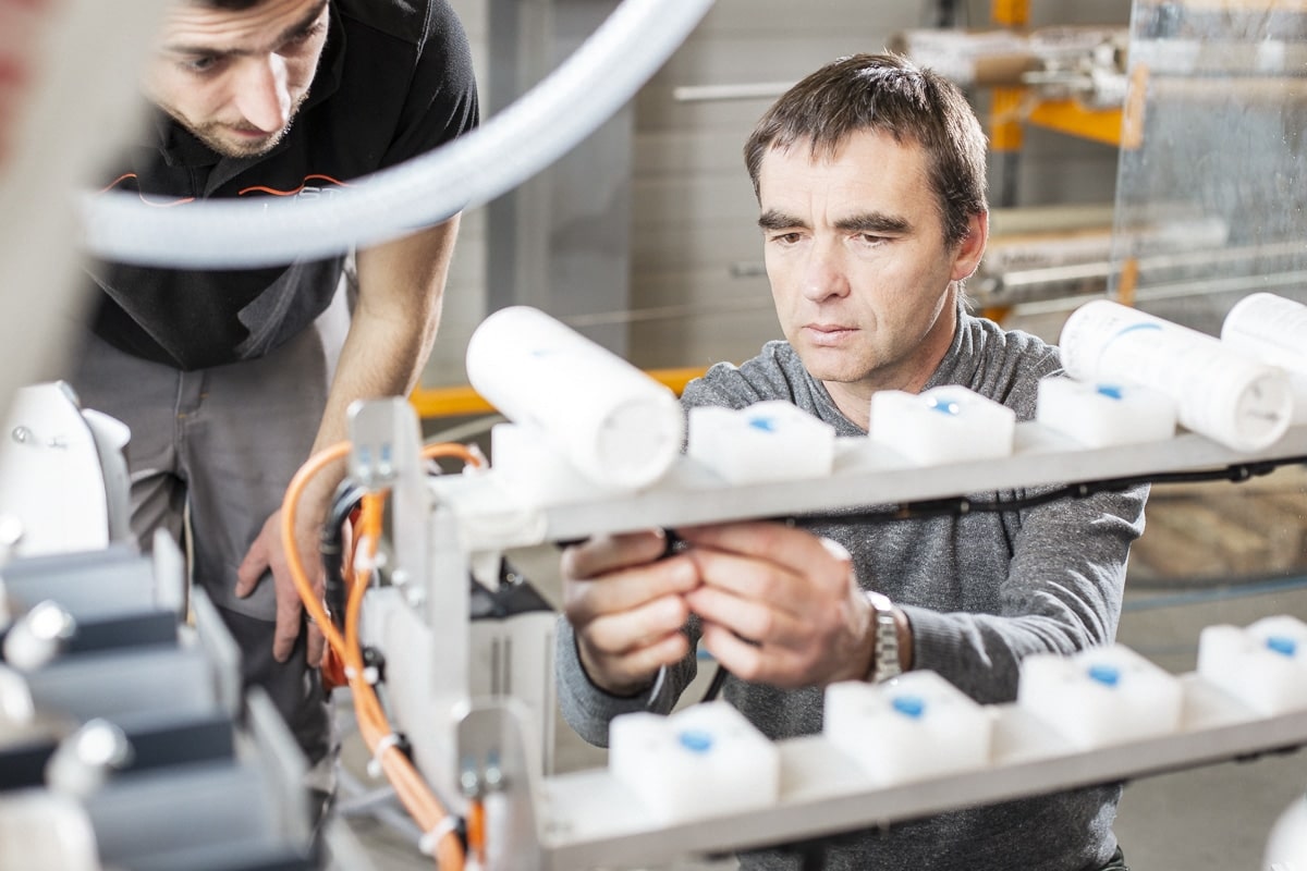 Deux techniciens concentrés sur l'ajustement d'une machine automatisée dans un environnement de production.