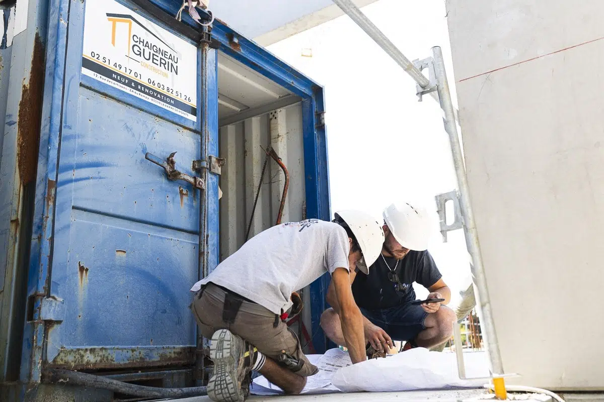 Deux ouvriers analysant des plans de construction devant une base de chantier à La Barre-de-Monts