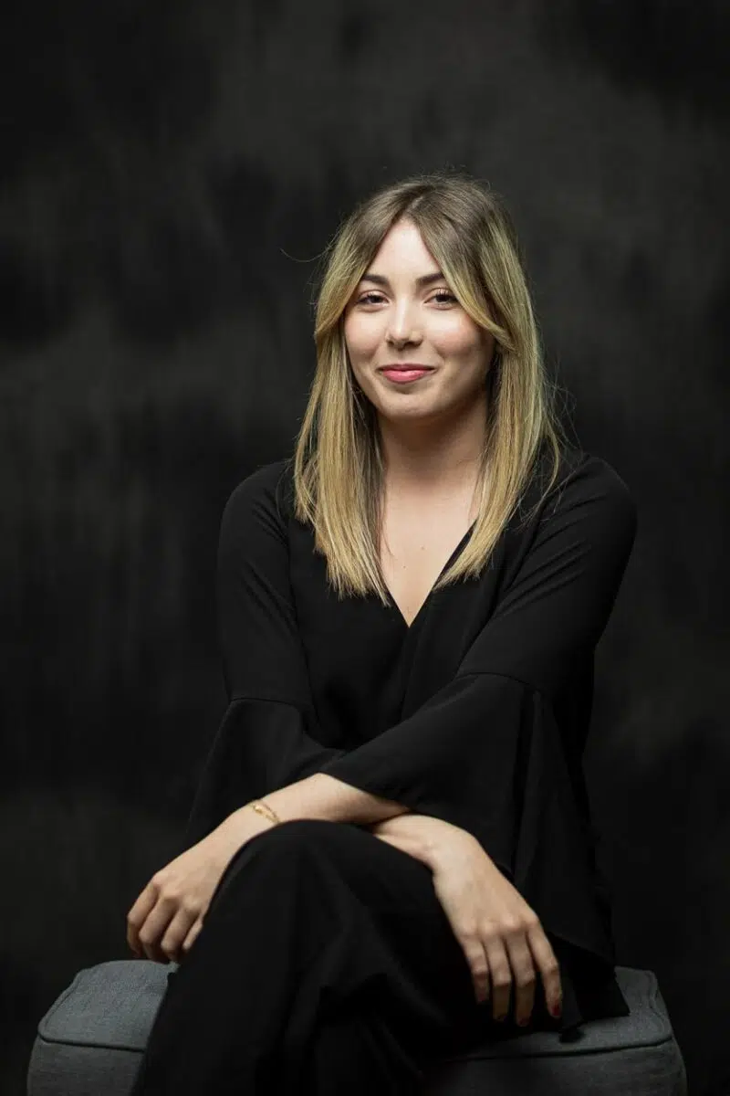 portrait femme blonde assise en vetement noire sur fond sombre