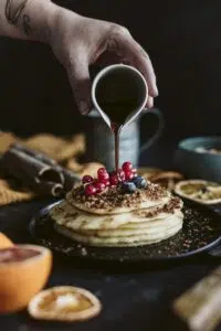 Une main vers un coulis sur des pancakes recouverts de fruits rouges